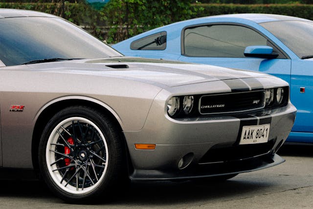 Close-up of a silver Dodge Challenger SRT parked next to a blue Ford Mustang in an outdoor setting.