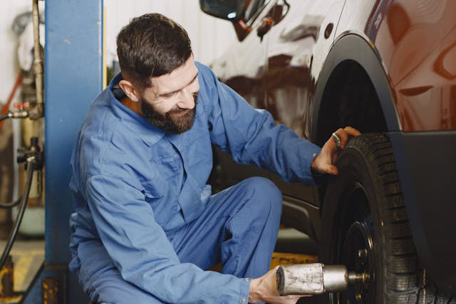 Mechanic in blue coveralls uses a power tool to change a tire on an orange vehicle in a garage.